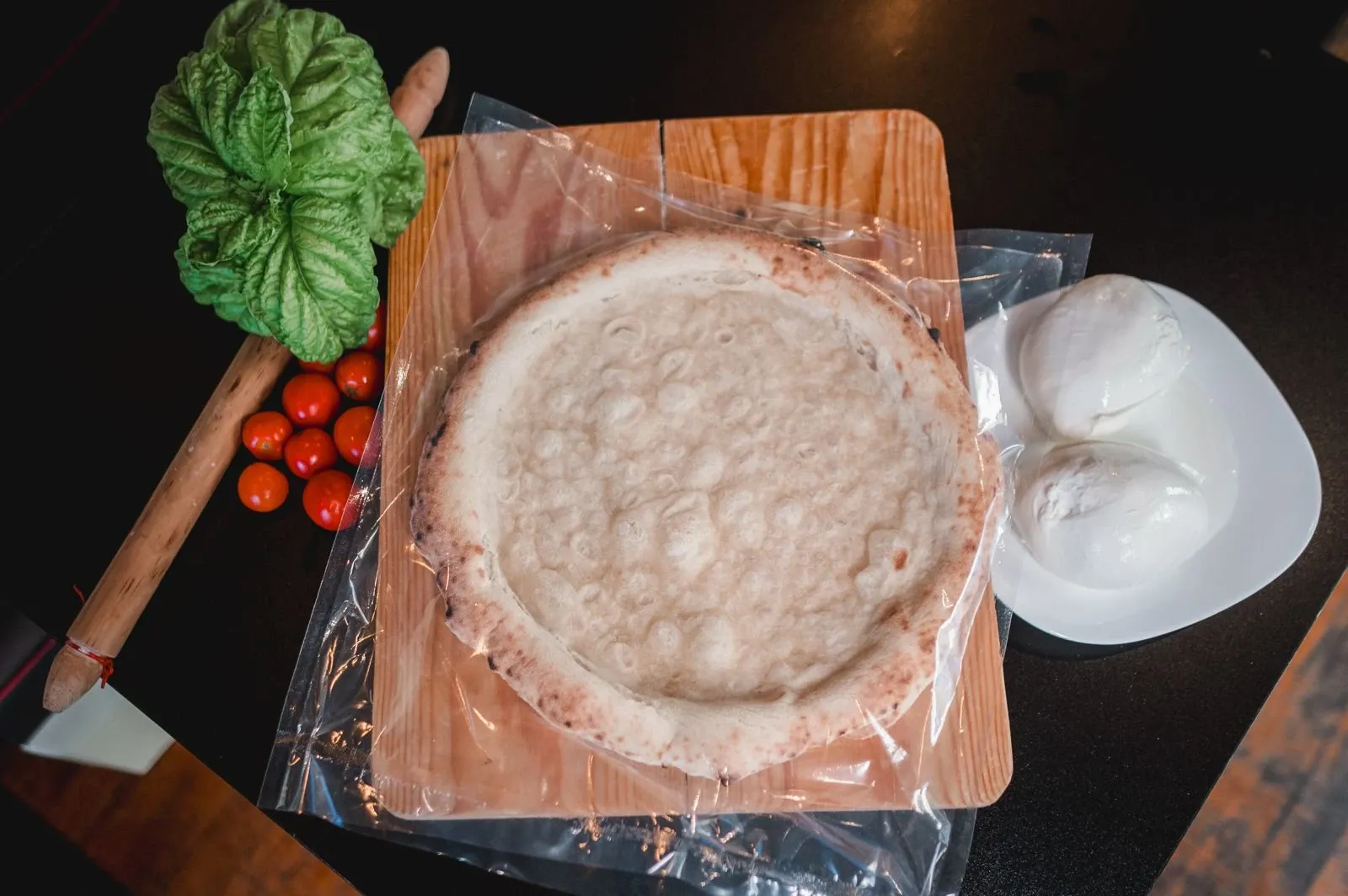 Fermento Pizzaboden in der Schutzgasverpackung, daneben Mozzarella, Tomaten und Basilikum