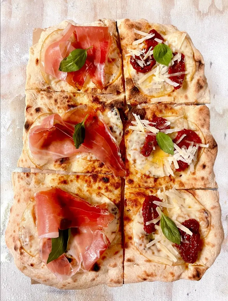 Pizza alla Pala in Stücken, belegt mit Rohschinken, Tomaten und Parmesan
